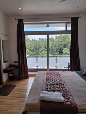 Un dormitorio con una cama grande, un escritorio y vistas a un lago a través de una puerta de vidrio.