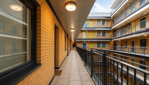 A corridor with a brick wall, a glass window, a tiled floor, and a railing. - Inclusive 1BR Central Abode w Parking and Balcony (Liverpool)