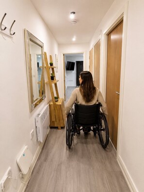 A person in a wheelchair in a hallway with a mirror, a radiator, and a door. - Inclusive 1BR Central Abode w Parking and Balcony (Liverpool)