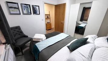 A hotel room with a bed, a chair, a desk, and a wardrobe. There are three framed pictures on the wall.