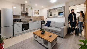 A modern kitchen with stainless steel appliances, a grey sofa, and a wooden coffee table.