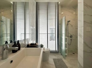 A modern bathroom with a bathtub, a shower, and a large window with blinds. - Luxury Five Star Condo Asoke Sukumvit, Downtown Area, one Large bed Room (Bangkok)