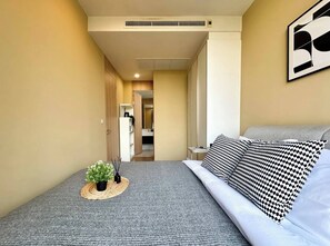 A bedroom with a bed, a bedside table, a wall-mounted artwork, and a potted plant. - Luxury Five Star Condo Asoke Sukumvit, Downtown Area, one Large bed Room (Bangkok)