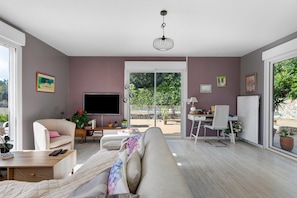 Ein modernes Wohnzimmer mit einer Couch, einem Fernseher und einem Essbereich mit einem Sessel und Tisch.