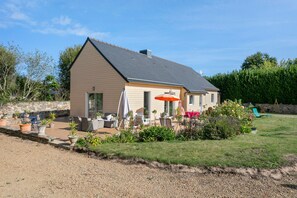 A single-story house with a sloped roof, a patio with outdoor furniture, and a garden area. - Holiday Home 'Maison Kerjean' with Shared Terrace, Private Garden and Wi-Fi (Plouha)