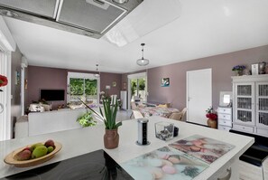 Eine moderne Küche mit einer zentralen Kochinsel, einem Essbereich mit Tisch und Blick ins Freie.