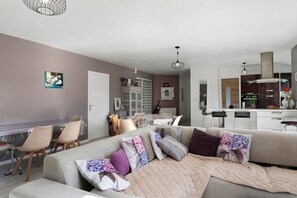A modern living room with a sofa, chairs, a dining area, and a kitchen in the background. - Holiday Home 'Maison Kerjean' with Shared Terrace, Private Garden and Wi-Fi (Plouha)