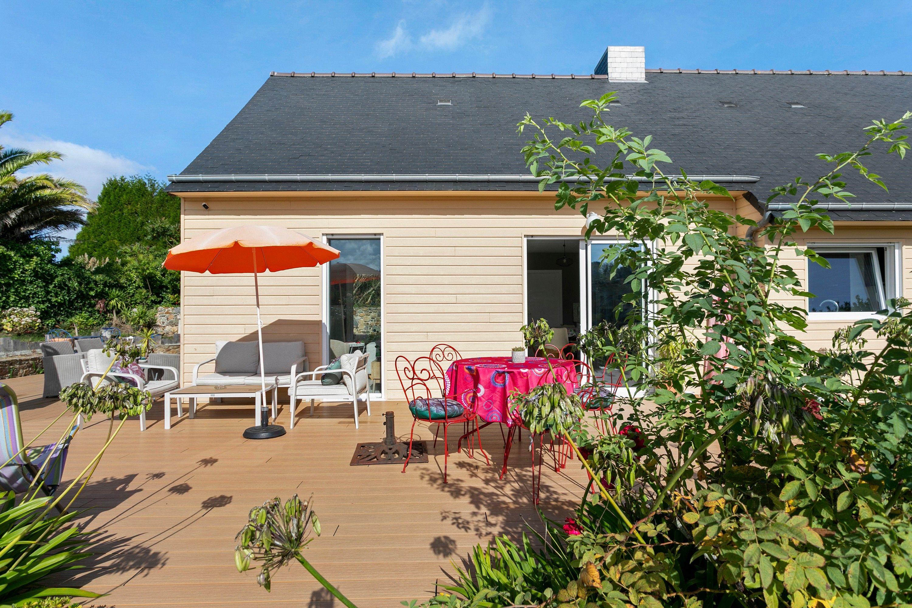 A house with a patio area featuring outdoor furniture, a table, and an umbrella.