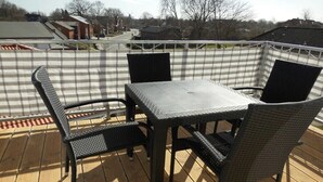 En terrasse med et bord og fire stole, omgivet af et hvidt og gråt stribet hegn.