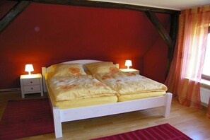 Habitación individual con una cama de madera, dos lámparas de noche, una pared roja y una ventana con cortinas.