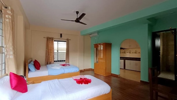 A hotel room with two beds, a ceiling fan, a kitchenette, and a bathroom with a shower curtain. - Hotel Forestway Hostel and Backpackers (Pokhara)