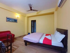 Un dormitorio con cama, sofá rojo, ventilador de techo y aire acondicionado instalado en la pared.