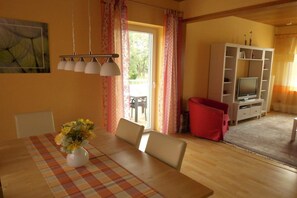 A dining area with a table, chairs, a vase of flowers, a television, and a cabinet. - The Comfortable Holiday Apartment (Kappeln)
