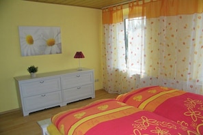 A bedroom with two beds, a white dresser, a potted plant, and a window with curtains. - The Comfortable Holiday Apartment (Kappeln)