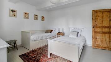 Een slaapkamer met twee eenpersoonsbedden, een houten garderobe, een klein krukje en een kamerkleed met dessin.