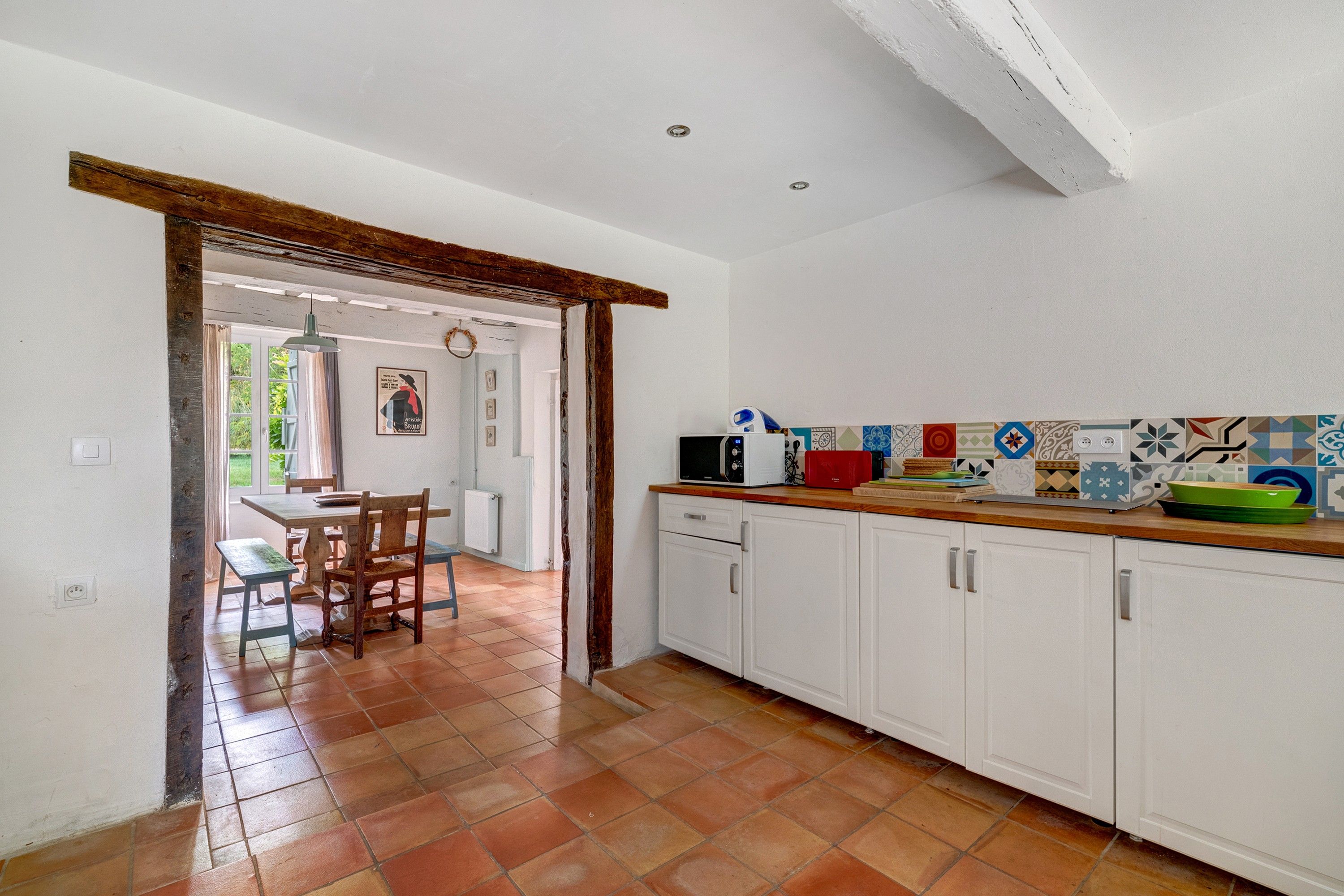 Cozinha com armários brancos, painel de azulejos e bancada de madeira.