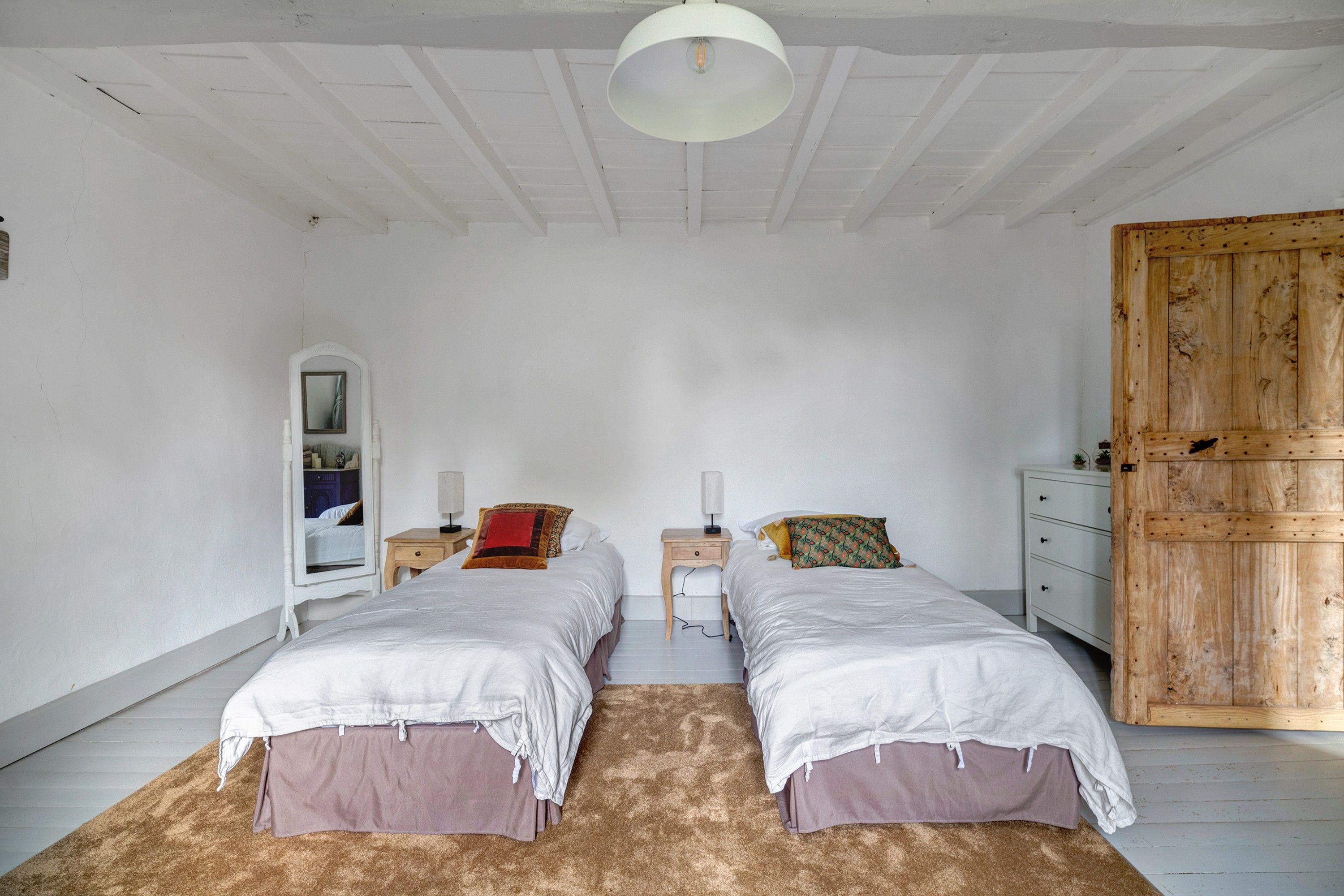 Quarto com duas camas, um guarda-roupa de madeira, um espelho e uma escrivaninha.