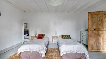 Quarto com duas camas, um guarda-roupa de madeira, um espelho e uma escrivaninha.