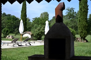 An outdoor seating area with a stone-built barbecue grill, two white umbrellas, and lounge chairs.