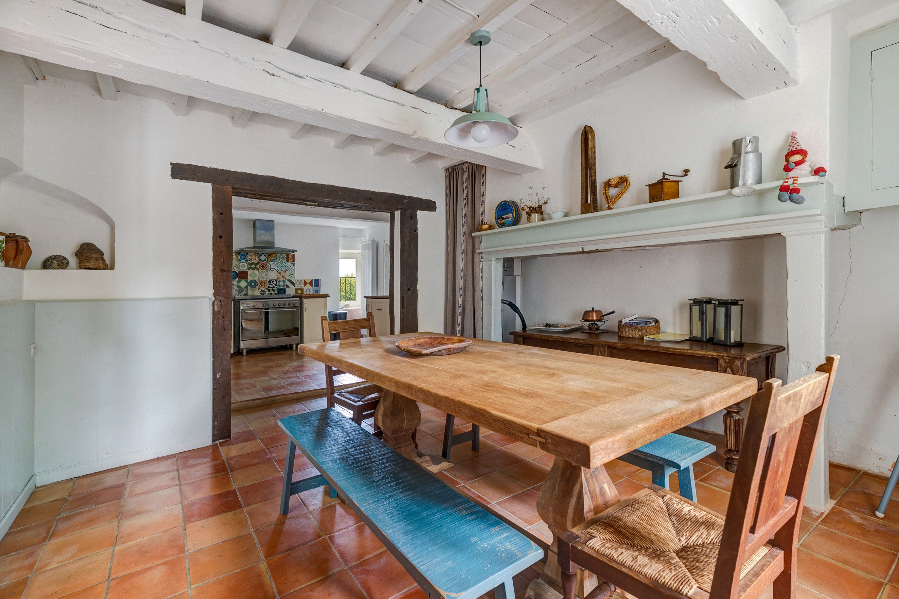 Una cocina rústica con una mesa de madera, bancos y piso de baldosas.