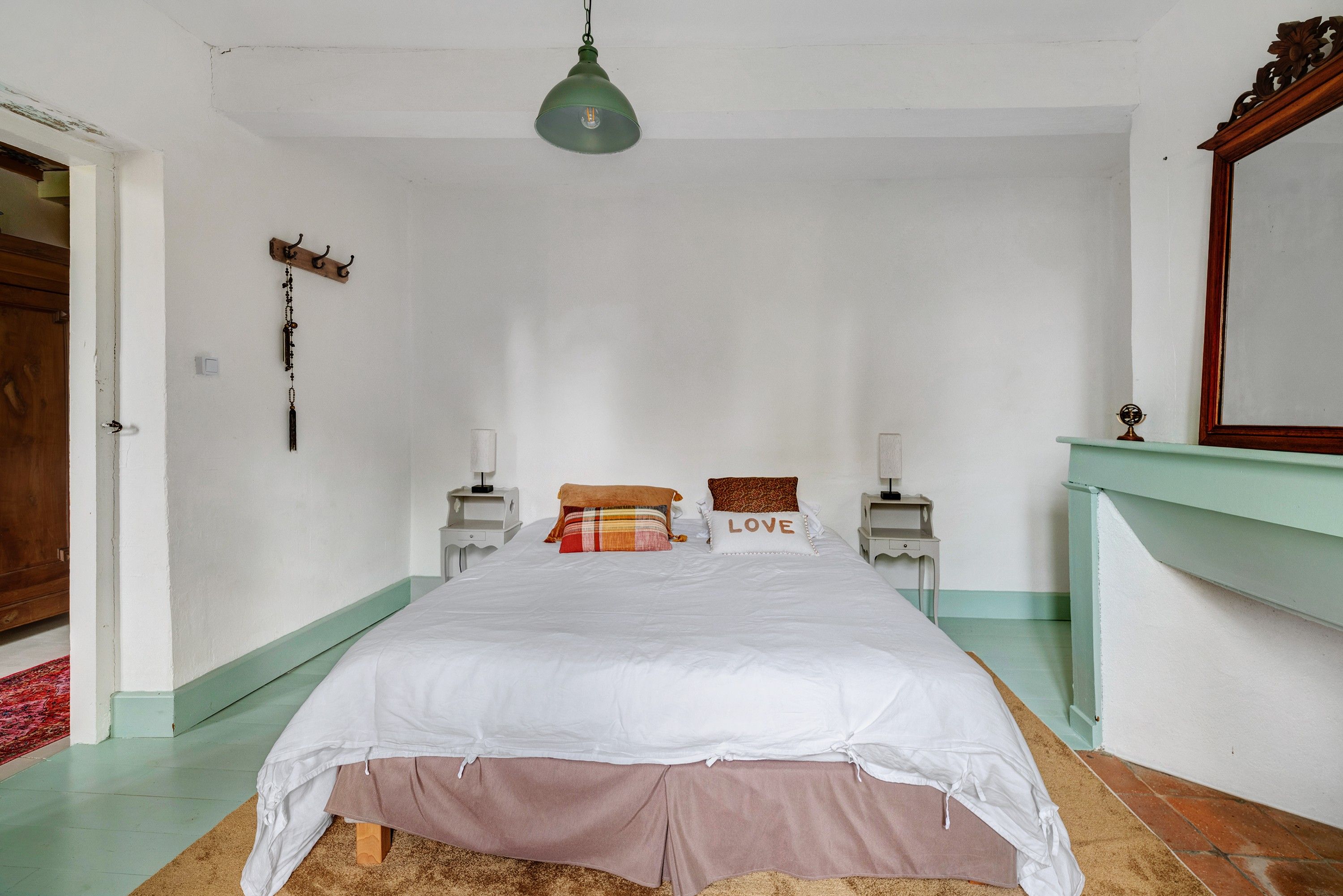Quarto com cama, mesas de cabeceira, luminária pendente, espelho e porta-roupas.