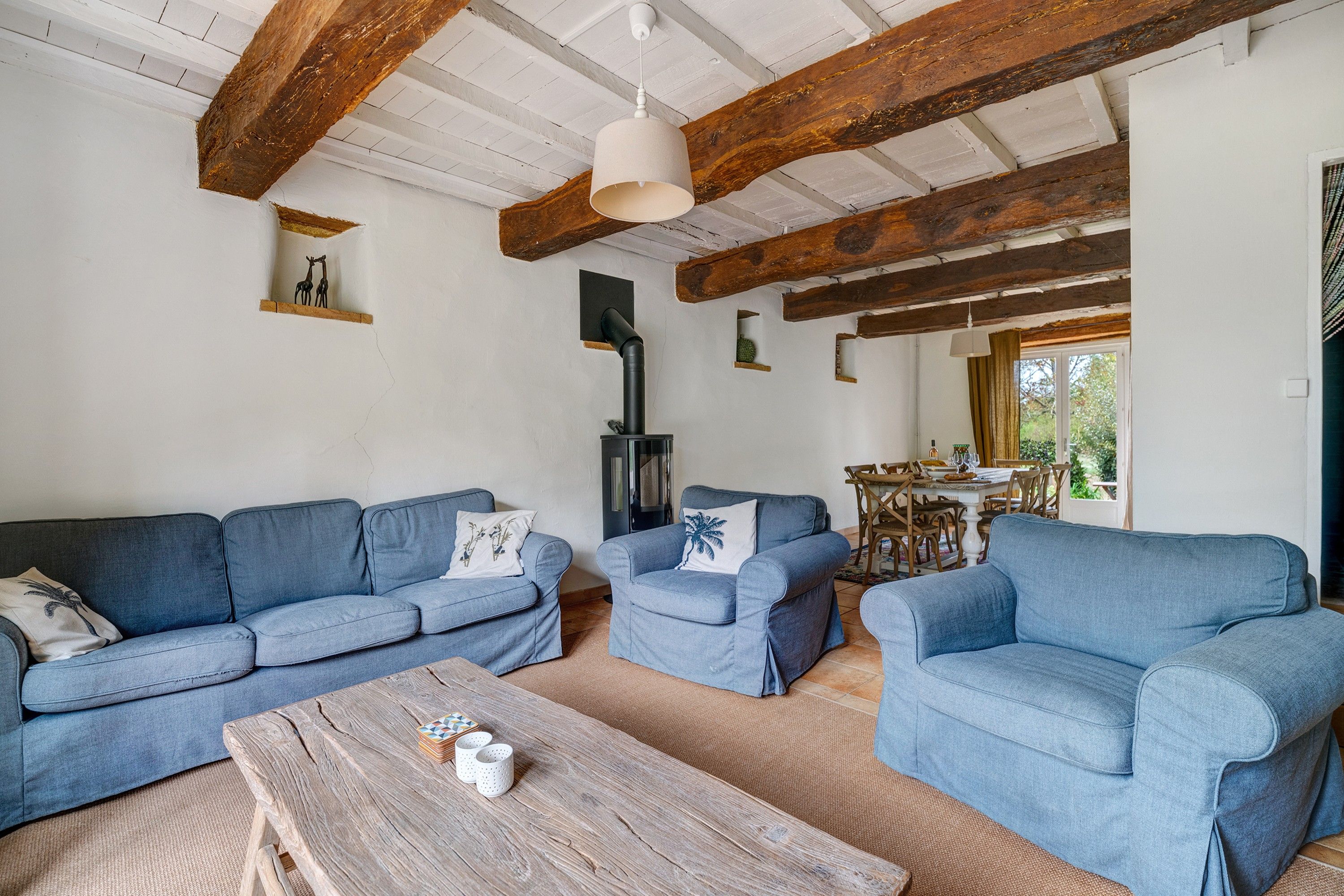 Ein Wohnzimmer mit Holzbalkendecke, Kamin und Essbereich mit Tisch und Stühlen.