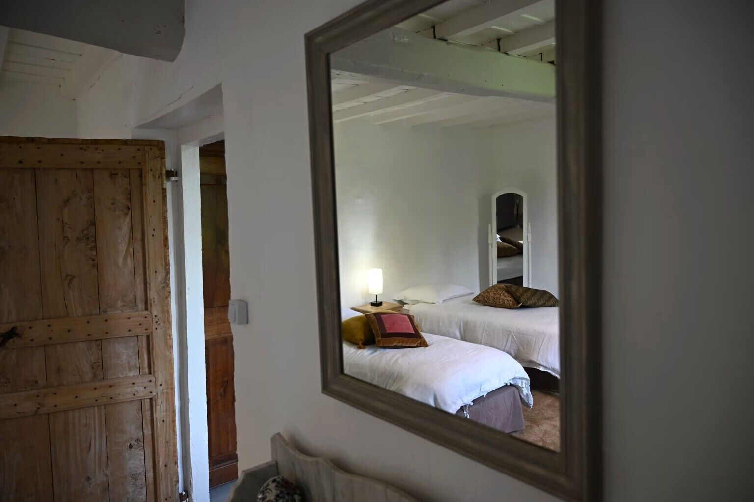 Een kamer met twee bedden, een houten deur en een spiegel die de kamer weerspiegelt.