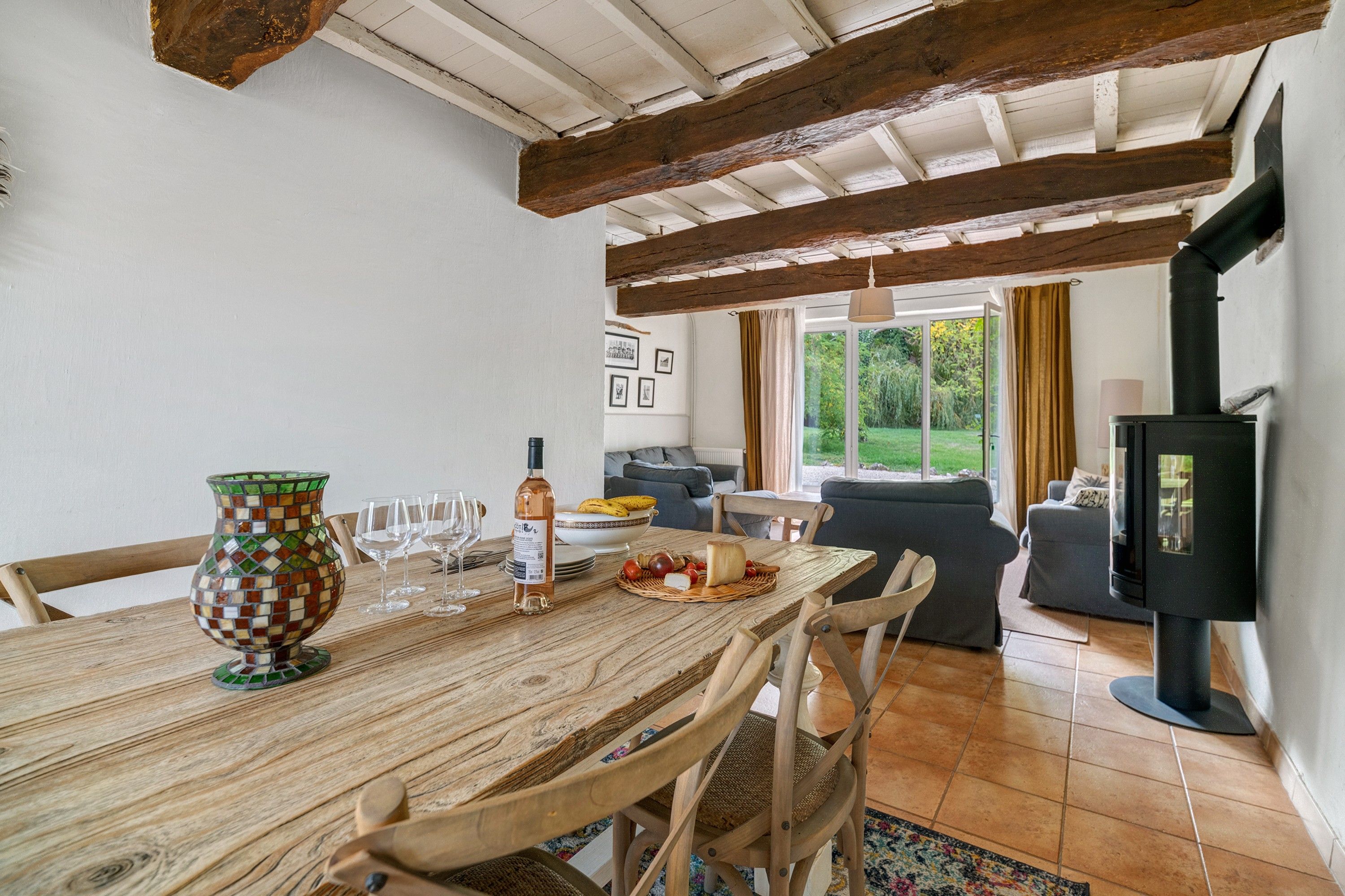Een eethoek met een houten tafel, stoelen, een mozaïekvaas, wijnglazen en een fles.