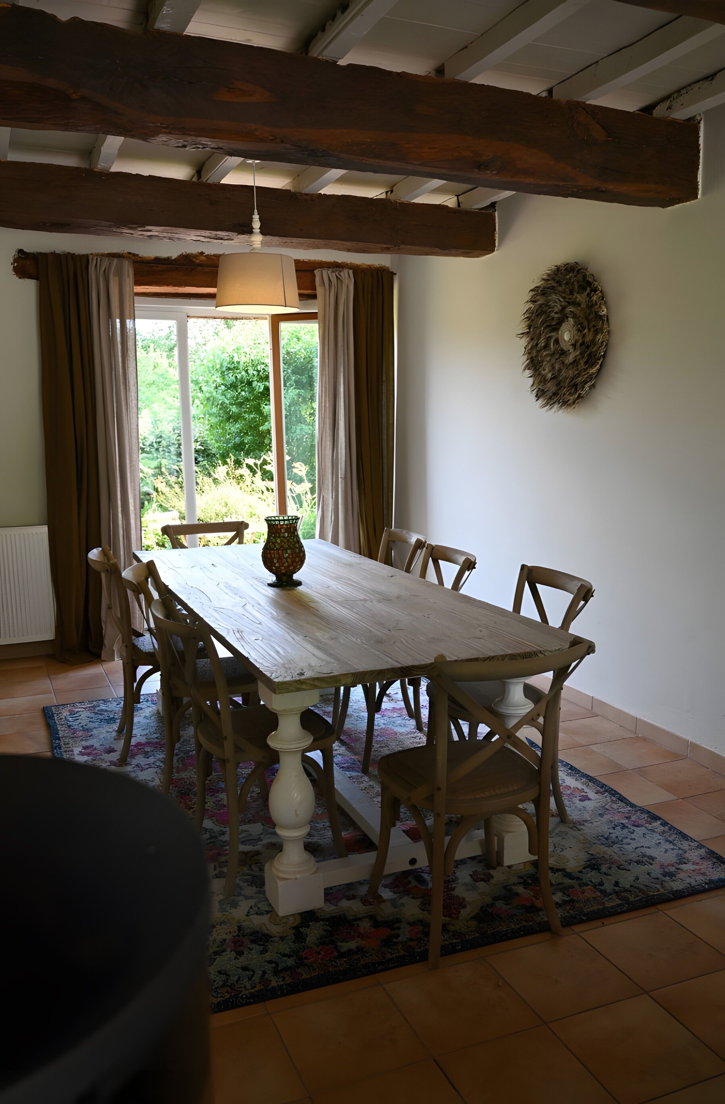 Een eethoek met een houten tafel en stoelen, een vaas, en uitzicht op groen buiten.