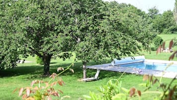 Piscina com área gramada e árvores ao fundo.