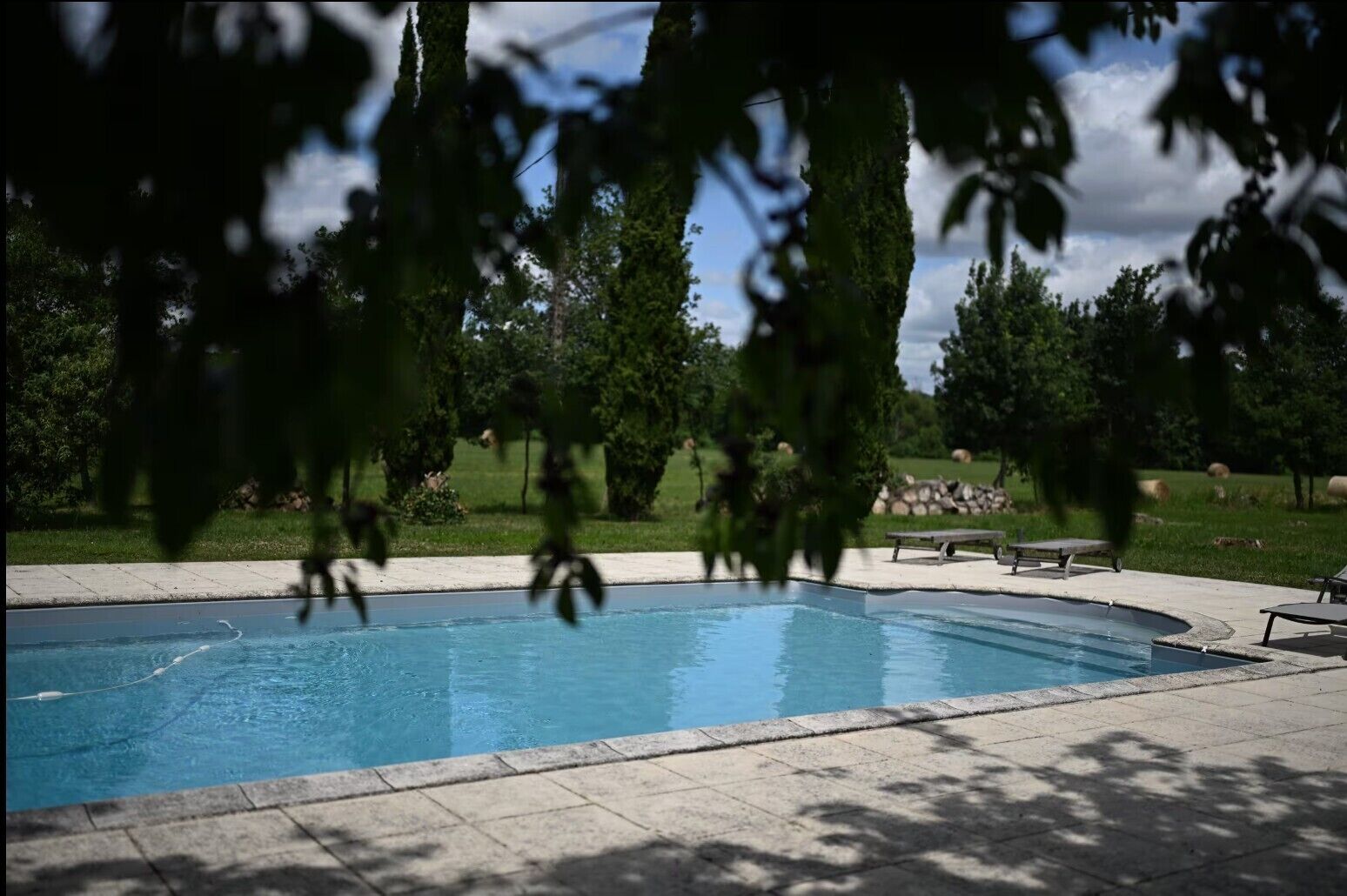 A swimming pool with a paved deck, surrounded by trees and a grassy area.