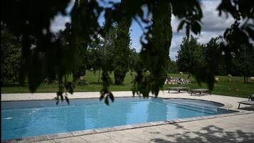 A swimming pool with a paved deck, surrounded by trees and a grassy area.