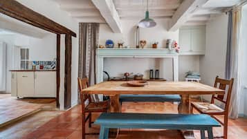 Uma cozinha rústica com uma mesa de madeira, cadeiras e um banco. Há um lustre pendurado sobre a mesa.