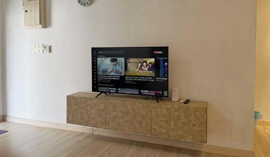 Una TV a schermo piatto su un supporto in legno, con una presa di corrente e una sveglia sopra.