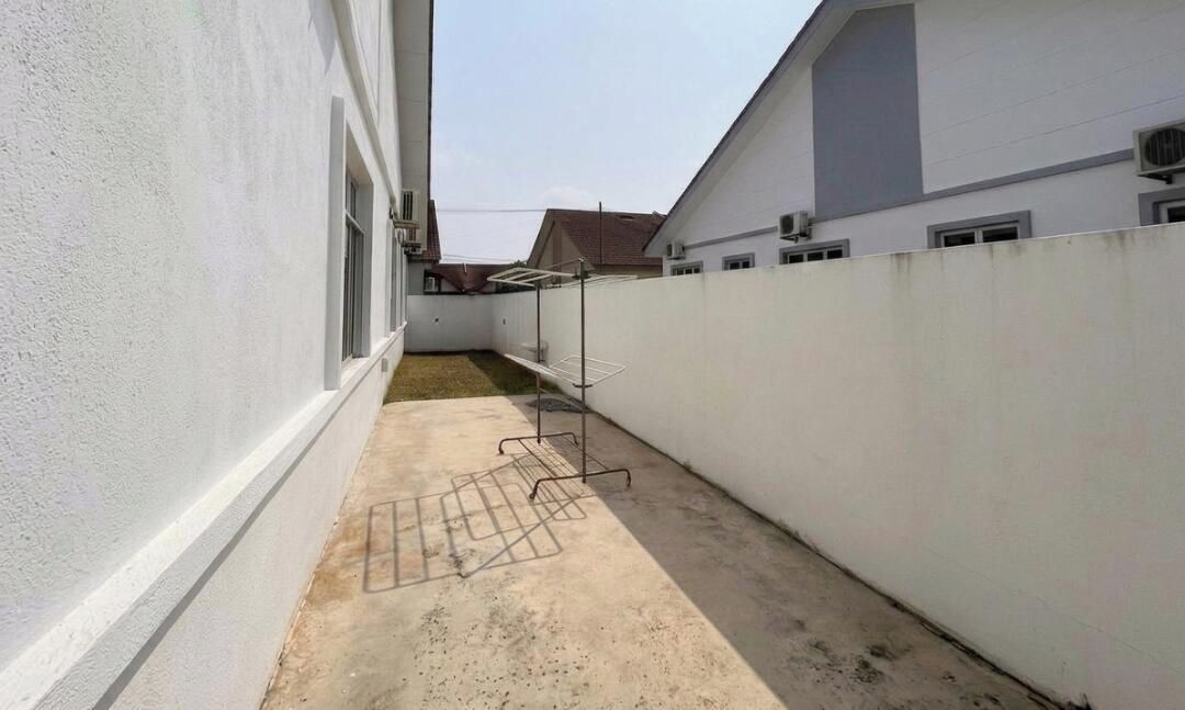 A narrow outdoor corridor with a concrete floor, a metal drying rack, and a white wall.