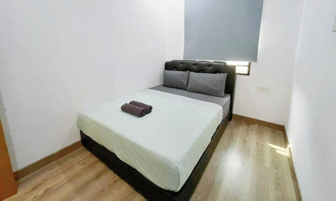 A small, single-bed room with a wooden floor, a grey headboard, and a bedside lamp.