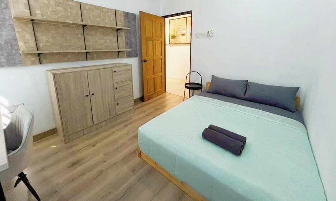 A bedroom with a bed, a wardrobe, a chair, and a door leading to another room.