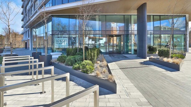 Een modern gebouw met een glazen gevel, terrasplekken en een aangelegde entree.