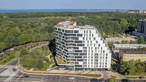 Un edificio moderno de varios pisos con techo plano, rodeado de abundante vegetación y vistas al mar.