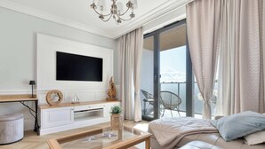 Een moderne woonkamer met een flatscreen televisie, een houten salontafel, een bank en een balkon met tuinmeubilair.