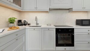 Een moderne keuken met witte kastjes, een ingebouwde oven, een magnetron en een koffiezetapparaat.