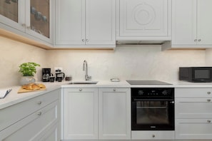 Una cocina moderna con armarios blancos, horno empotrado, microondas y cafetera.