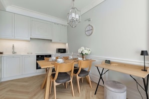 Una cocina moderna con armarios blancos, una mesa de comedor lista para cuatro personas y un reloj fijado a la pared.