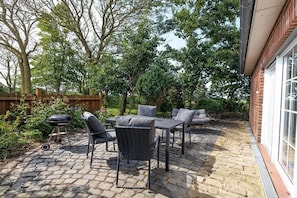An outdoor patio with a brick floor, a table with chairs, and a barbecue grill. - Holiday apartment with 1 bedroom (Westerdeichstrich)