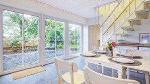 A dining area with a table set for two, a staircase, and a view of the outdoors through large sliding doors. - Holiday apartment with 1 bedroom (Westerdeichstrich)