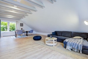 A modern living room with a dark sofa, round coffee table, and a dining area with chairs and a table. - Holiday apartment with 1 bedroom (Westerdeichstrich)