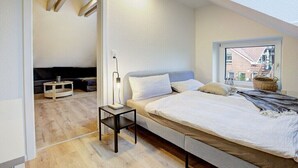 A bedroom with a bed, bedside table, lamp, and a view through a window. - Holiday apartment with 1 bedroom (Westerdeichstrich)