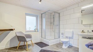 A modern bathroom with a glass-enclosed shower, a toilet, a sink, and a chair. - Holiday apartment with 1 bedroom (Westerdeichstrich)