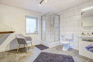 Un bagno moderno con doccia vetro, un water, un lavandino e una sedia.