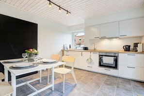 A modern kitchen with white cabinetry, a built-in oven, and a dining area with a table set for four. - Holiday apartment with 1 bedroom (Westerdeichstrich)